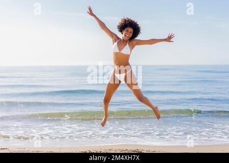 Giovane donna allegra che salta davanti al mare nelle giornate di sole Foto Stock