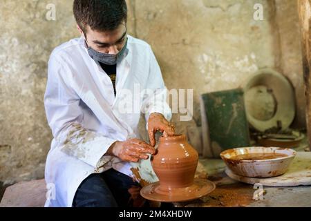 Artigiano che indossa maschera di protezione che fa pentola su ceramica ruota Foto Stock