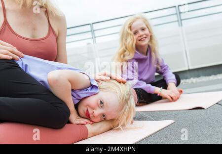 Figlia sorridente sdraiata in grembo della madre in terrazza Foto Stock