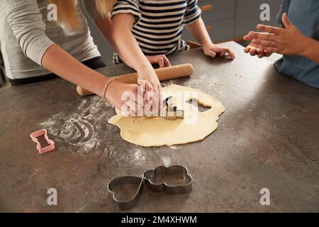 Le mani dei bambini che usano il taglierino per biscotti al bancone della cucina Foto Stock