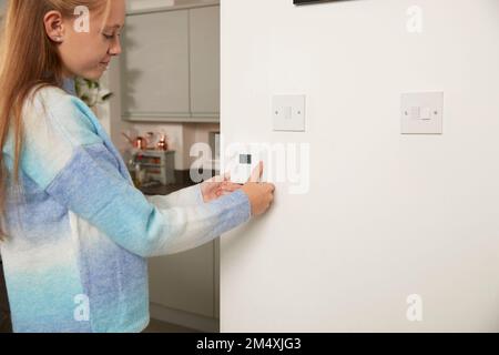 Ragazza sorridente che regola il termostato sulla parete a casa Foto Stock