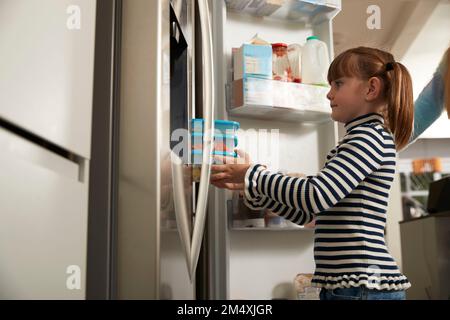 Ragazza che tiene contenitori di plastica in frigorifero a casa Foto Stock