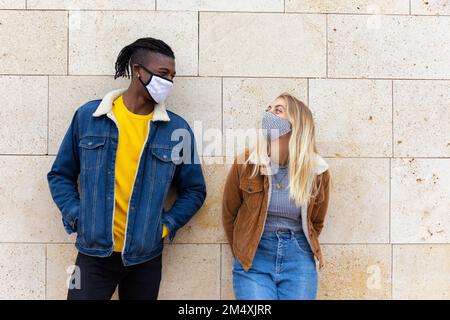 Giovani amici che indossano maschere protettive davanti al muro Foto Stock