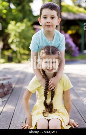 Ragazzo sorridente con sorella seduta in giardino Foto Stock