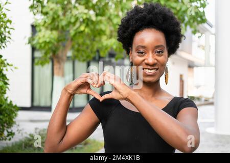 Donna sorridente che fa un gesto cardiaco con le mani Foto Stock