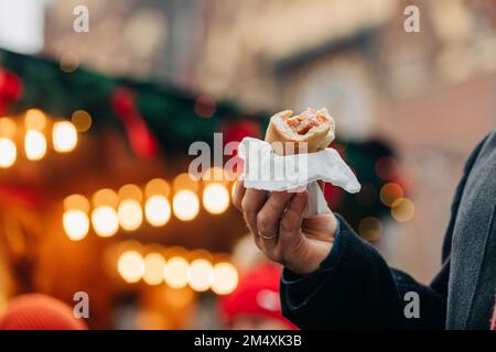 Mano dell'uomo che tiene il cane caldo al mercato di Natale Foto Stock