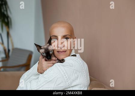 Donna senza capelli matura che abbraccia Sphynx gatto sul divano Foto Stock