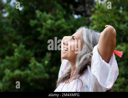 Felice donna matura con le mani dietro la testa nella foresta Foto Stock