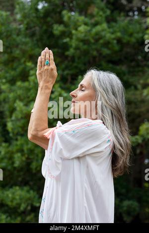 Donna matura meditando con le mani aggrappate nella foresta Foto Stock