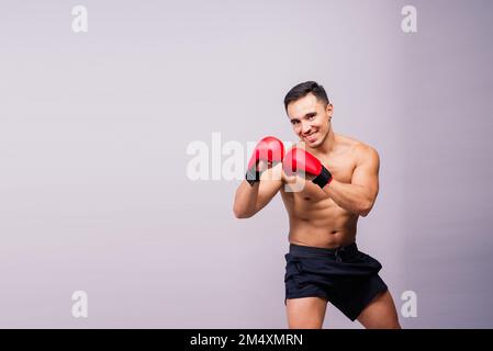 Modello muscolare sportivo giovane uomo in guanti da boxe su sfondo grigio. Maschio che flette i suoi muscoli. Foto Stock