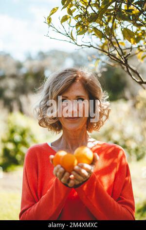 Donna sorridente che tiene frutti d'arancia in giardino Foto Stock