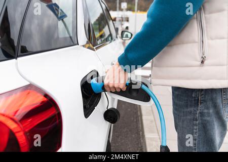 Uomo che collega il caricabatterie all'auto elettrica Foto Stock