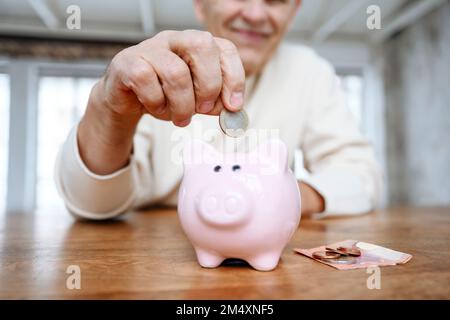 L'uomo che mette la moneta nella banca del piggy nel paese Foto Stock