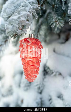 Cono di pino arancione appeso su ramo di albero di Natale coperto di neve Foto Stock