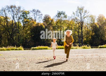 Giocosa donna anziana che corre con la nipote nel parco Foto Stock