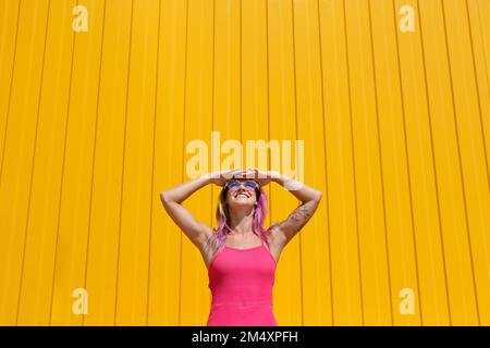 Donna felice che indossa gli occhi schermanti di vestito rosa davanti alla parete gialla Foto Stock