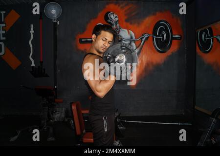Un uomo del Sud asiatico che fa bicipiti in palestra Foto Stock