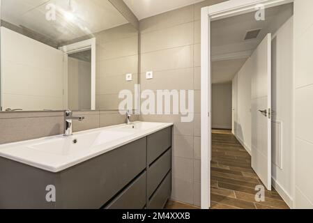 Bagno con armadi in legno grigio con cassetti e doppio lavabo in porcellana sotto un grande specchio rettangolare senza cornice Foto Stock