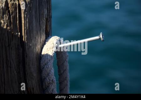 Corda appesa su un chiodo in un palo di ormeggio presso la riva di un lago visto da vicino Foto Stock