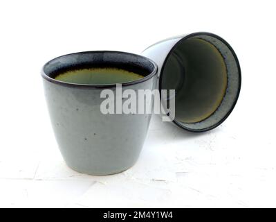 Due tazze in ceramica senza manico su sfondo bianco. Occhiali grigi lucidi. Primo piano vuoto della tazza blu fatta a mano. Stoviglie per caffè e casa. Foto Stock