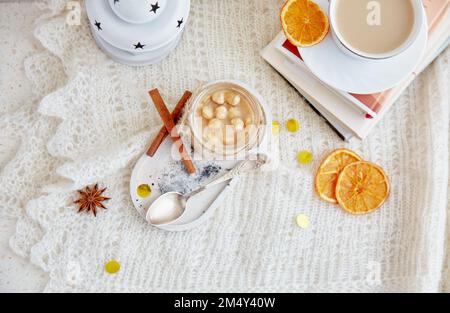 Natale accogliente prima colazione. Caramello salato di nocciola fatto in casa spalmato in vaso di vetro, candele, libri e tazza di caffè piatto. Foto Stock