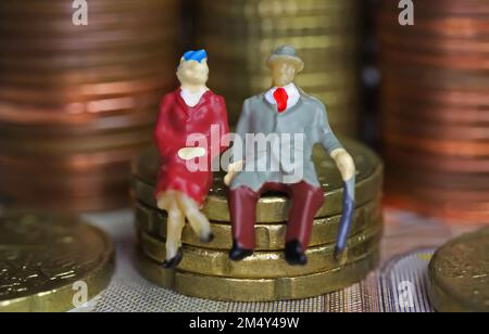 Abstract figure isolate di una coppia anziana in pensione seduta su una pila di monete in euro - concetto di pensione e risparmio pensionistico Foto Stock