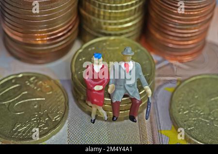 Abstract figure isolate di una coppia anziana in pensione seduta su una pila di monete in euro - concetto di pensione e risparmio pensionistico Foto Stock