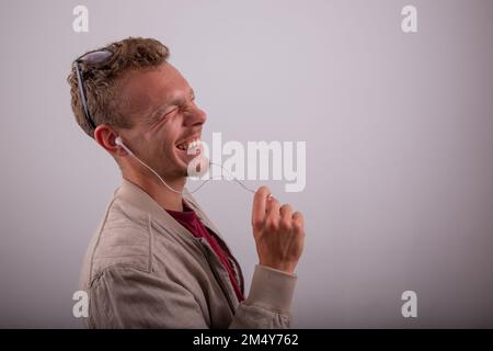 Un uomo ride mentre ascolta un audio con le sue cuffie, studio girato con uno sfondo bianco Foto Stock