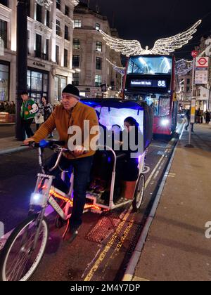 Rickshaw, aka Tuk-tuk, aka Pedicab, e gli spiriti di Natale, aka Angeli, sospesi sopra Regent Street come parte dell'esposizione delle luci di Natale. Londra Foto Stock