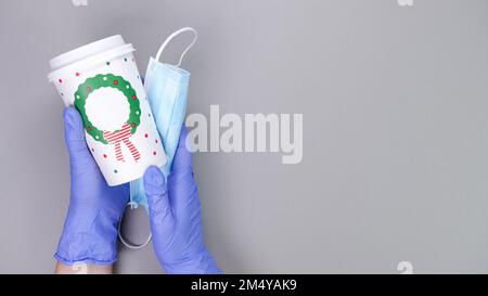 Mani in guanti blu protettivi con maschera medica tiene la tazza di carta da caffè su sfondo grigio con spazio copia. Protezione da virus. Infermiere, medico, barista, Foto Stock