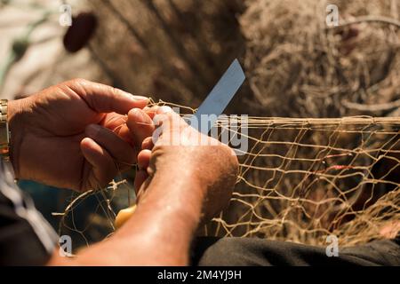 mani di pescatore con reti e coltello per la riparazione Foto Stock