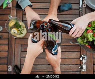 Heres a noi. Inquadratura ad angolo alto di un gruppo di persone non riconoscibili che tengono le bottiglie di birra e brindano all'esterno intorno a un tavolo. Foto Stock