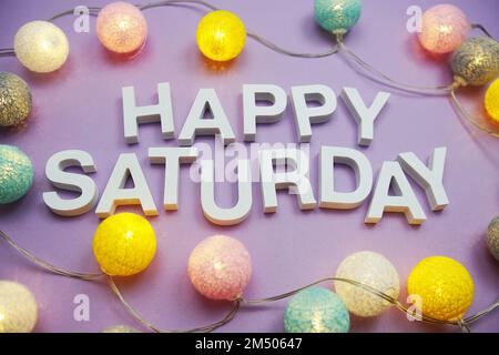 Lettere dell'alfabeto Happy Saturday con palle di cotone LED su sfondo viola Foto Stock