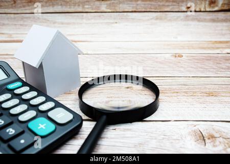 White Model House con lente d'ingrandimento e calcolatrice su sfondo in legno, concetto immobiliare Foto Stock