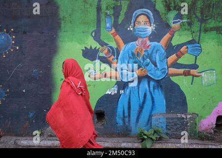 Una donna sari-placcata passa la pittura a tema Covid-19 parete nella zona di Biculla di Mumbai, India, raffigurante un'infermiera come una dea indù multi-armata Foto Stock