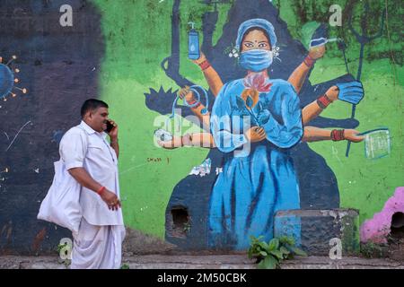 Un uomo passa il dipinto a tema Covid-19 nella zona di Biculla / Nagpada di Mumbai, India, raffigurando un'infermiera come una dea indù multi-armata Foto Stock