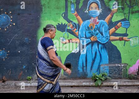 Una donna sari-placcata passa la pittura a tema Covid-19 parete nella zona di Biculla di Mumbai, India, raffigurante un'infermiera come una dea indù multi-armata Foto Stock