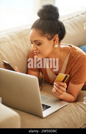 Prenotare online può essere un compito comodo e conveniente. una bella giovane donna che usa un computer portatile e una carta di credito a casa. Foto Stock