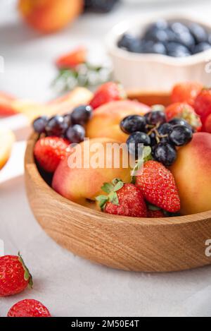 Bacche estive fresche e biologiche e frutti di fragole, mirtilli, pesche e uva in un piatto di legno su fondo bianco. Macro e primo piano. Foto Stock