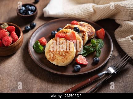 Frittelle al formaggio casolare con menta, mirtilli e fragole su uno sfondo di legno scuro. Colazione sana e deliziosa. Foto Stock