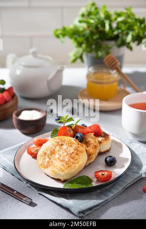 Frittelle con formaggio casolare o sciroppi con frutti di bosco freschi, miele e panna acida su fondo di mattone bianco sfocato con una tazza di tè. Il concetto di Foto Stock