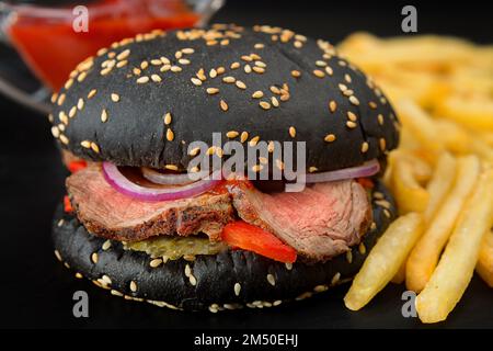 Hamburger nero con carne arrosto e verdure, con patate e salsa su sfondo sfocato Foto Stock
