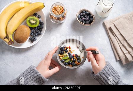 al bambino viene servita la colazione con yogurt abbondante e salutare con muesli, frutta fresca e frutti di bosco. Vista dall'alto. Foto Stock