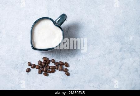 Una tazza di cappuccino a forma di cuore con grani sparsi su fondo blu. Vista dall'alto e spazio di copia. Foto Stock