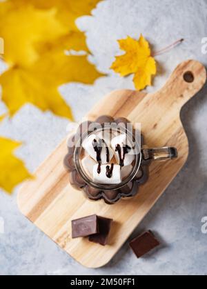 una tazza di cioccolata calda con marshmallows su un tagliere su sfondo blu. Concetto autunnale di una bevanda calda. Vista dall'alto e primo piano. Foto Stock