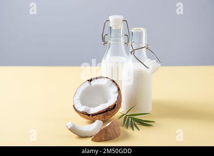 Concetto di consumo consapevole. Due bottiglie di latte vegano con semi-noci di cocco su fondo giallo e grigio. Vista frontale e immagine dello spazio di copia Foto Stock