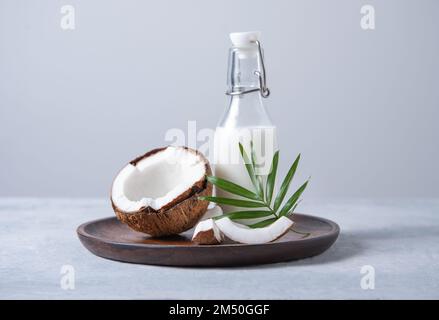Bottiglia di latte sana con semi di cocco e rametto di palma in piatto di legno su sfondo blu. Vista frontale e immagine dello spazio di copia Foto Stock