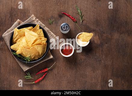 Piatto adagiare con tradizionali nachos di granoturco messicani con salsa e salsa alla panna, erbe, sale e peperoncino su fondo di legno. Vista dall'alto e copia Foto Stock