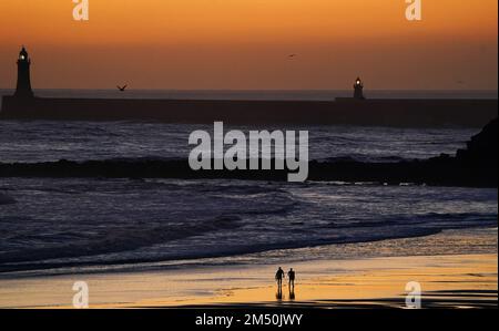 I surfisti camminano attraverso la spiaggia durante l'alba la vigilia di Natale camminano alla spiaggia di Tynemouth LongSands nel Nord Est dell'Inghilterra. Data immagine: Sabato 24 dicembre 2022. Foto Stock