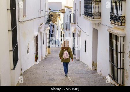 Donna sulla schiena che cammina attraverso un tipico villaggio andaluso di case bianche e bar di metallo sulle finestre, Medina Sidonia, Cadice. Foto Stock